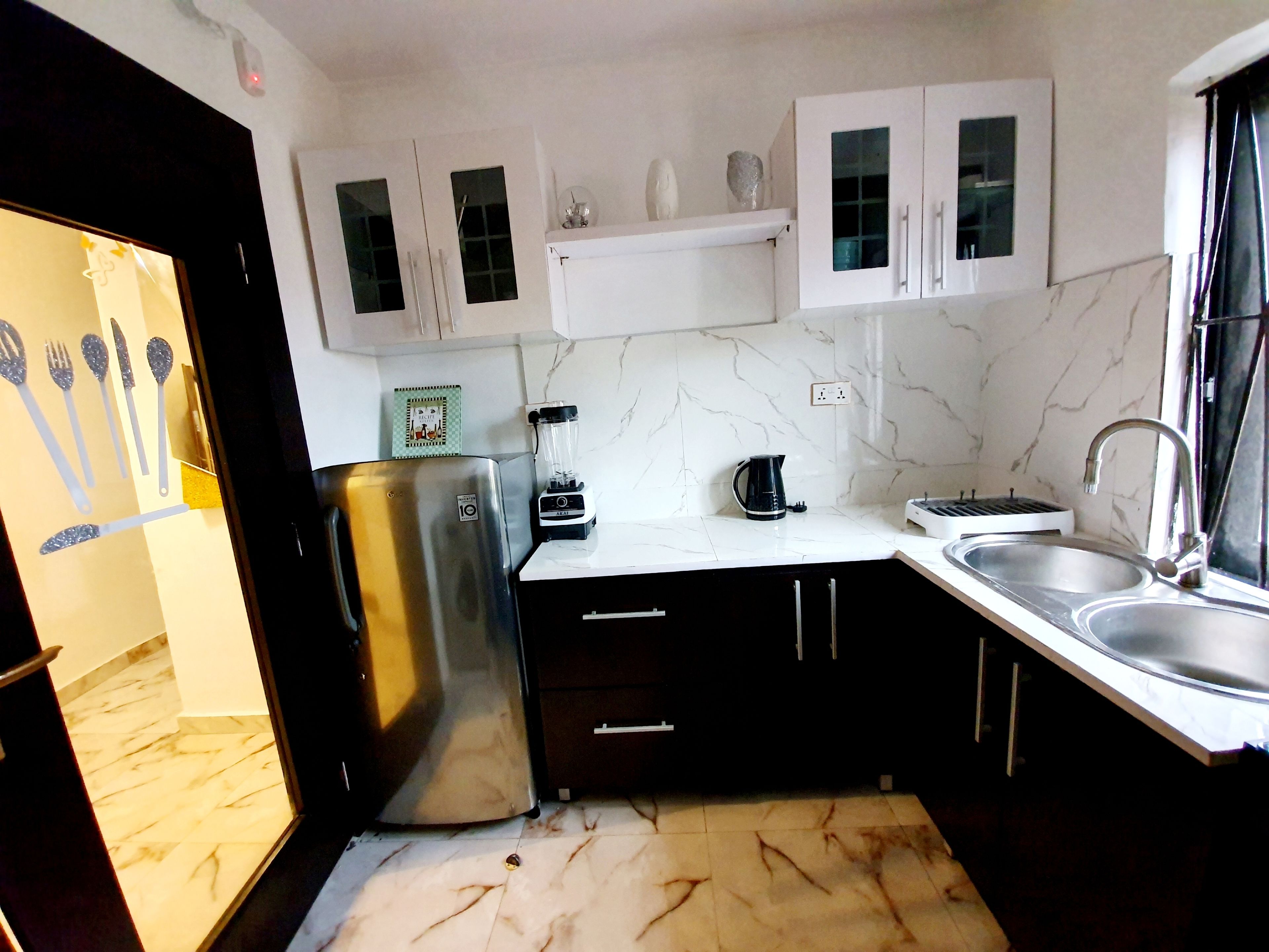 Una cocina con armarios blancos, un refrigerador de acero inoxidable, una cafetera y un lavamanos.