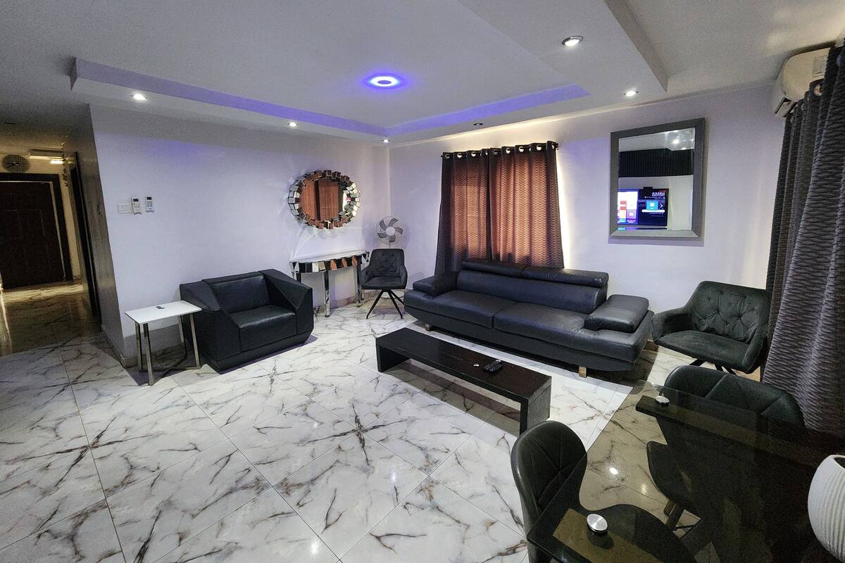 Una sala de estar moderna con un sofá, sillones, una mesa de centro y un televisor montado en la pared.