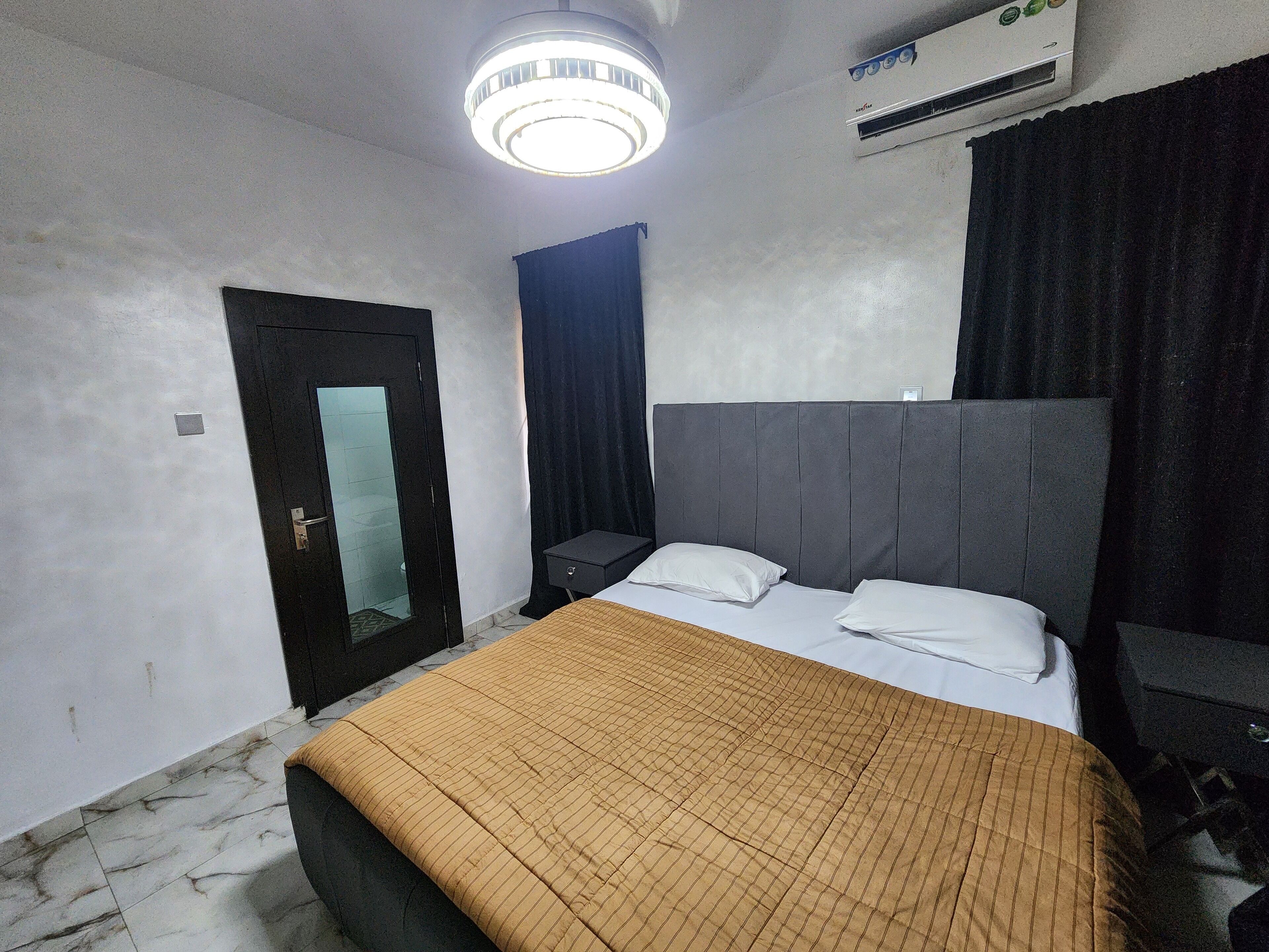 A hotel room with a bed, a nightstand, a wardrobe, a door, and an air conditioning unit.