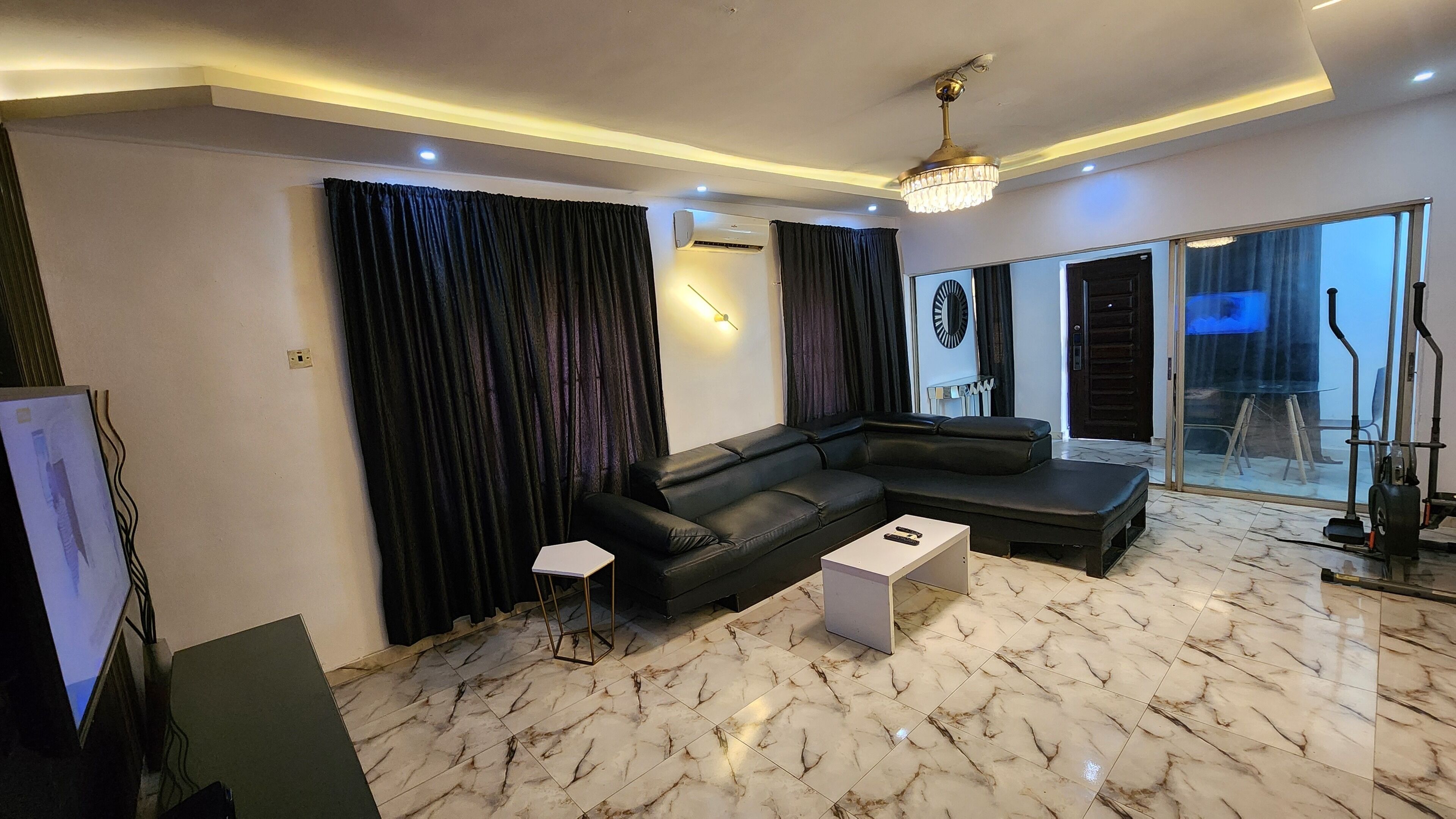 A modern living room with a black leather sofa, a white coffee table, and a large window with curtains.