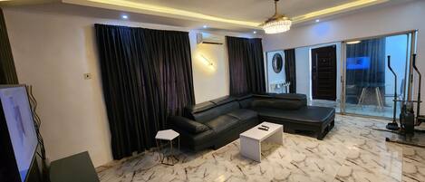 A modern living room with a black leather sofa, a white coffee table, and a large window with curtains.