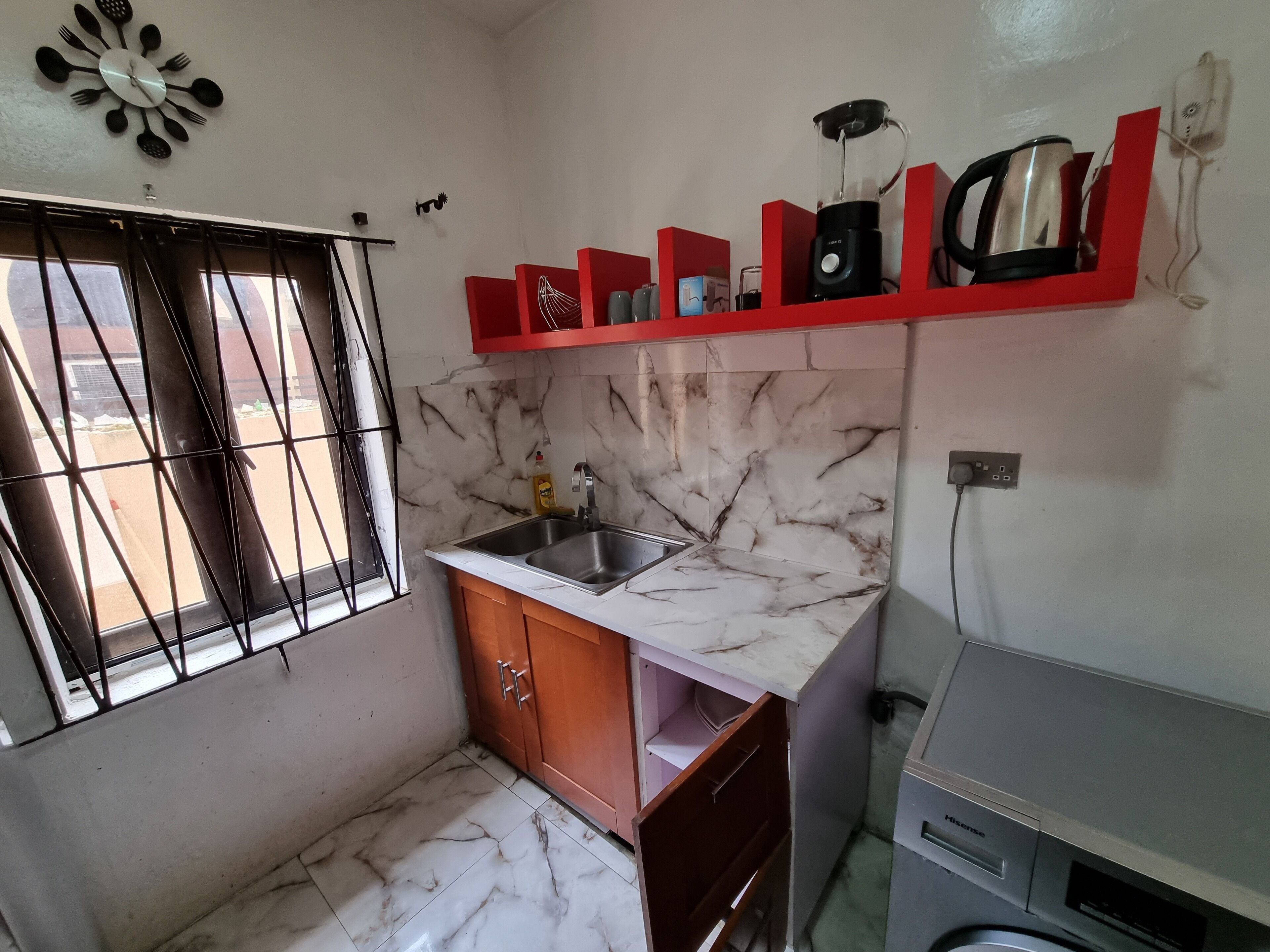 A compact kitchen with a marble backsplash, a sink, and a red shelf with kitchen appliances.