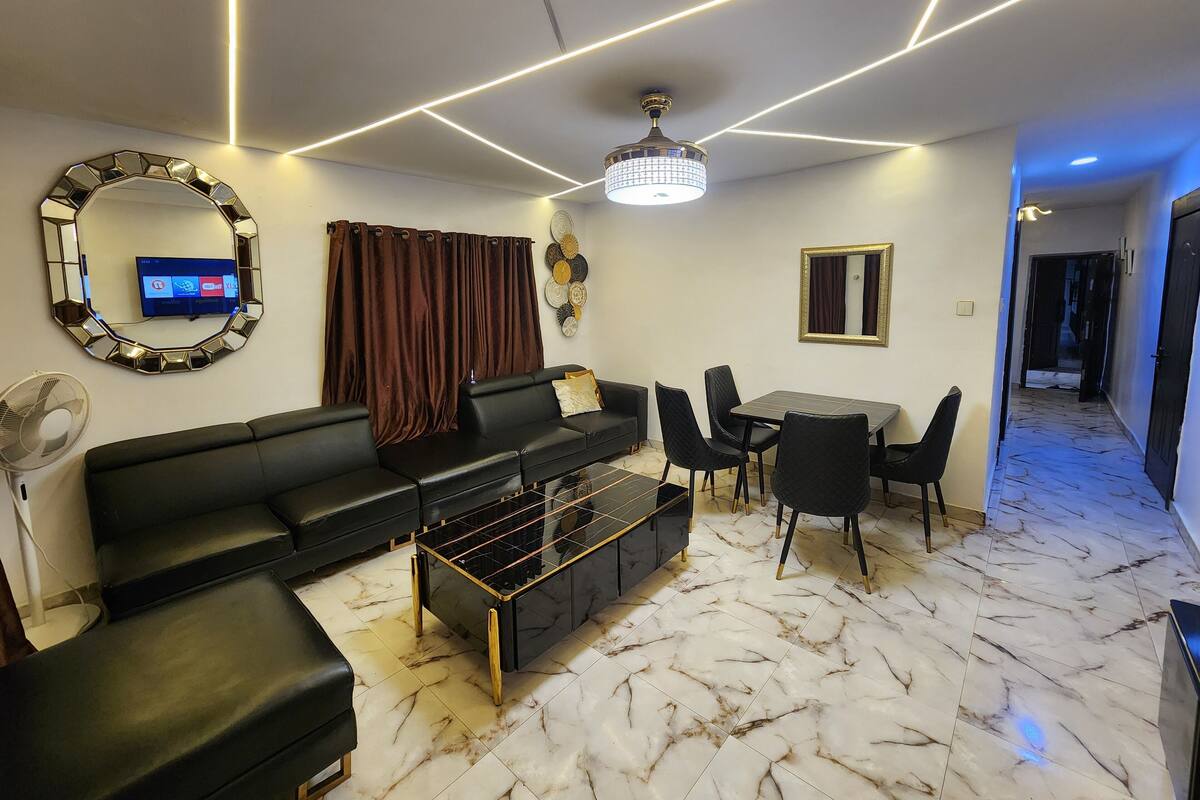 Una sala de estar moderna con un sofá negro, una mesa de centro de vidrio y un comedor con mesa y sillas.