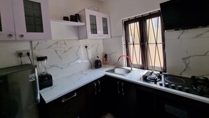 Une cuisine avec des carreaux de marbre blanc, un réfrigérateur noir, une cuisinière et des placards aux portes en verre.