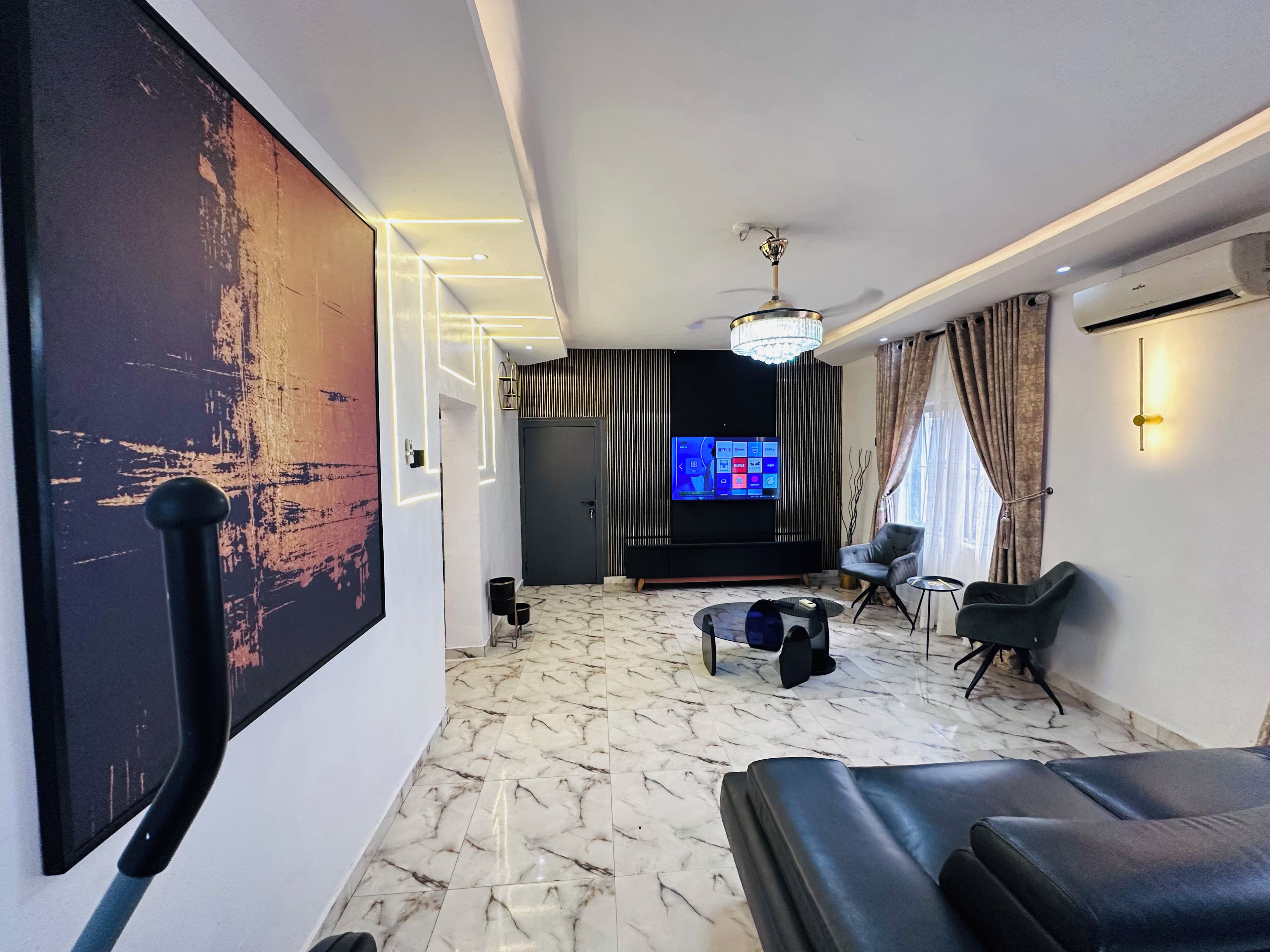 A modern living room with a large flat-screen TV, a ceiling fan, and a marble floor.