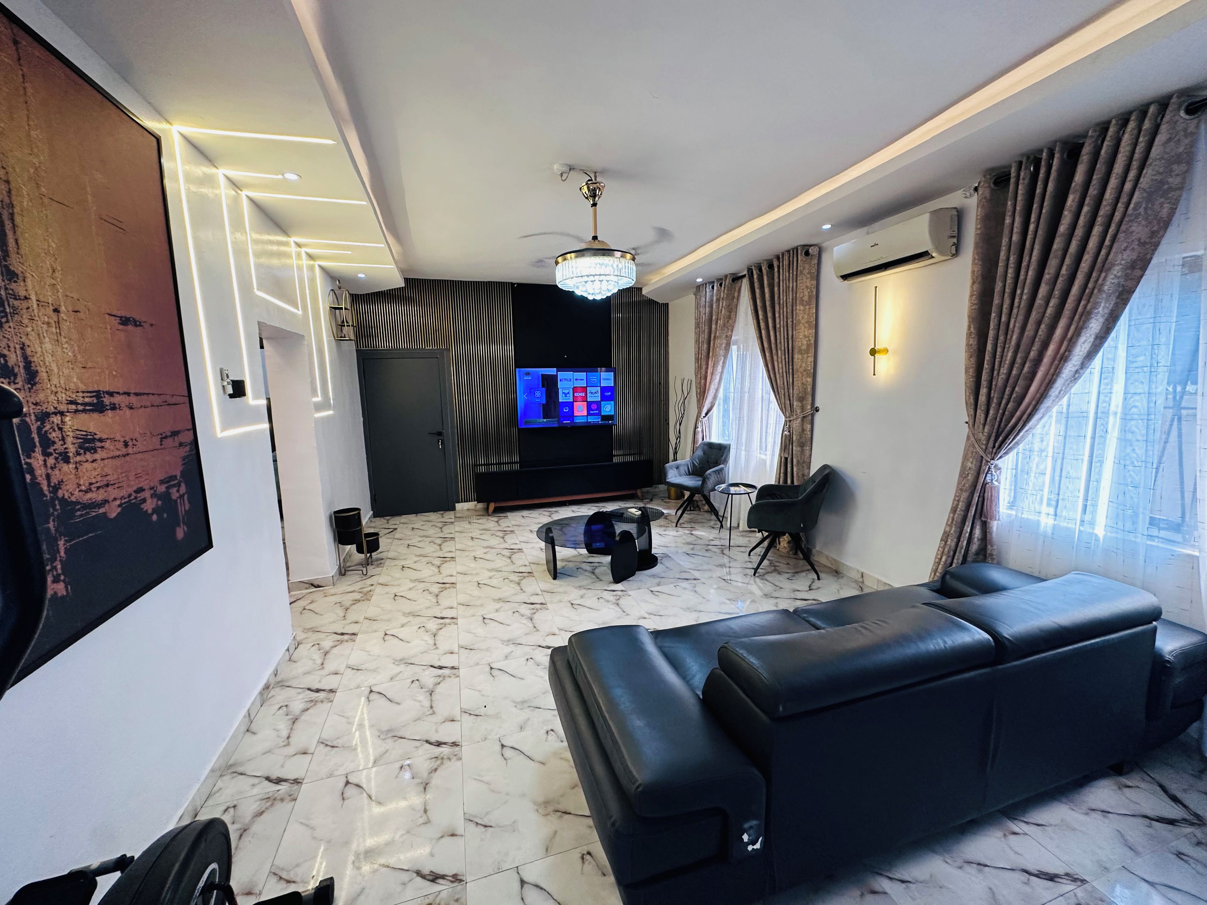A modern living room with a black leather sofa, a TV, and a ceiling fan.