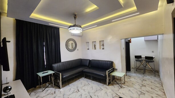 Un salon moderne avec un canapé d’angle, une petite table, un miroir décoratif et un coin repas avec des chaises.