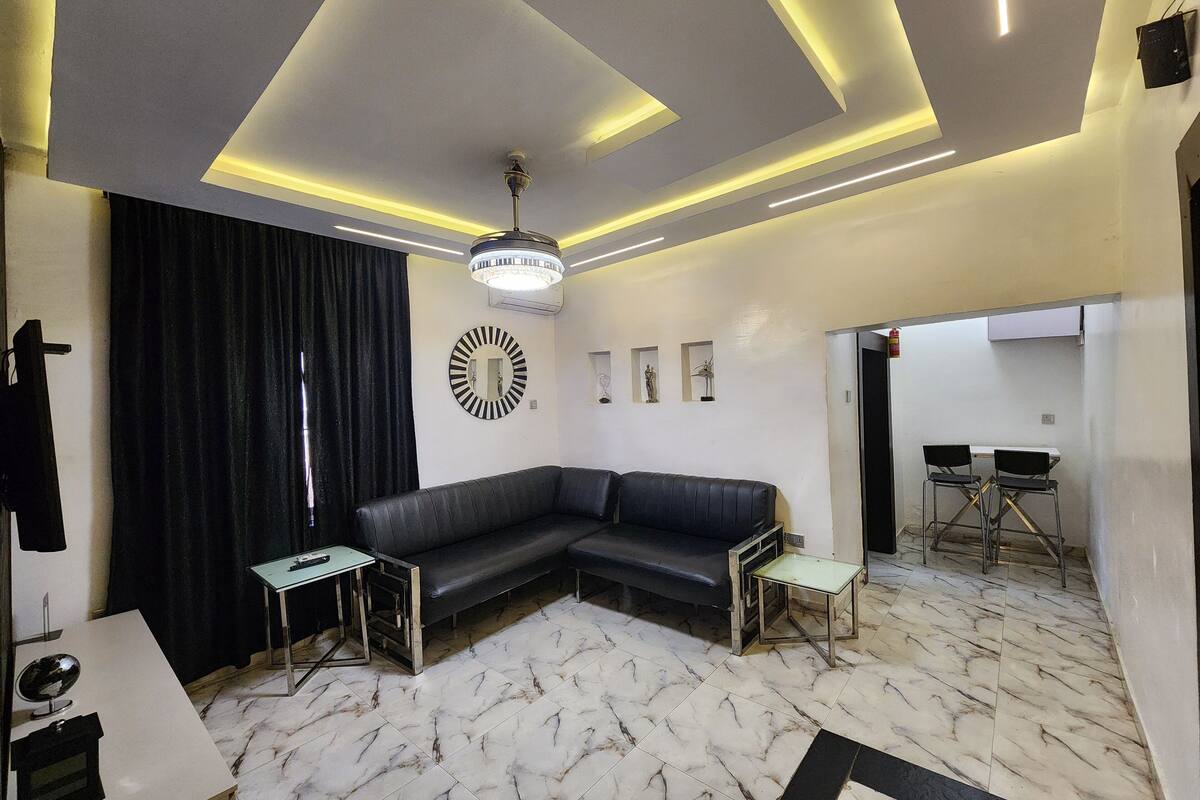 Una sala de estar moderna con un sofá seccional, una mesita, un espejo decorativo y un comedor con sillas.