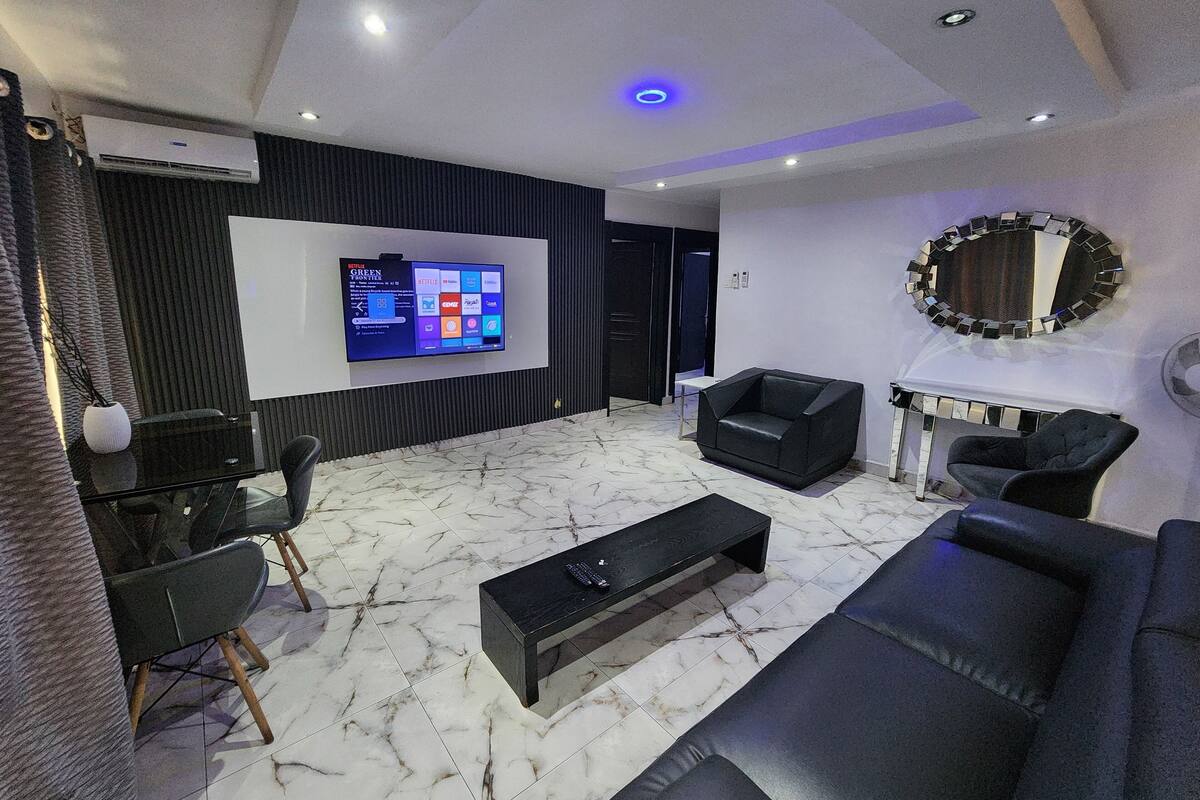 Una sala de estar moderna con televisor de pantalla plana, sofá de cuero negro y piso de mármol.