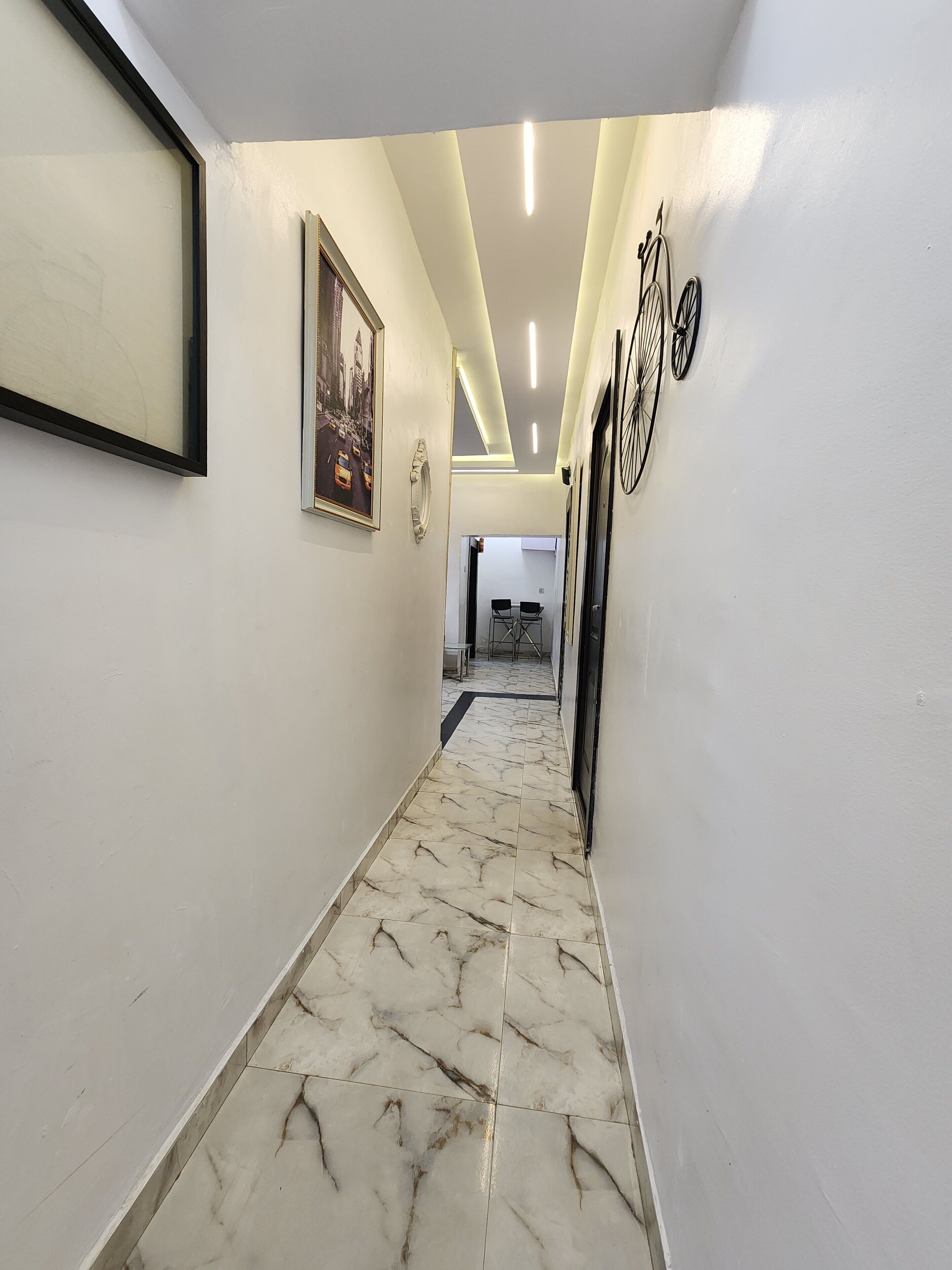 A hallway with marble flooring, framed artwork on the walls, and a bicycle rack.