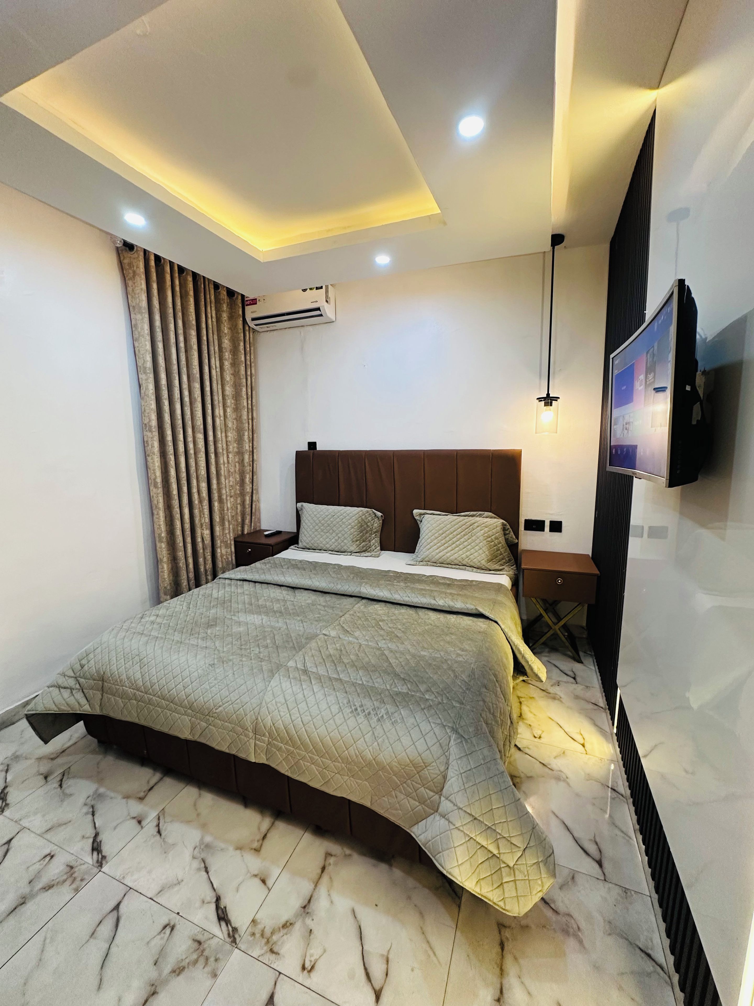 A modern bedroom with a bed, air conditioning unit, and a mounted television.