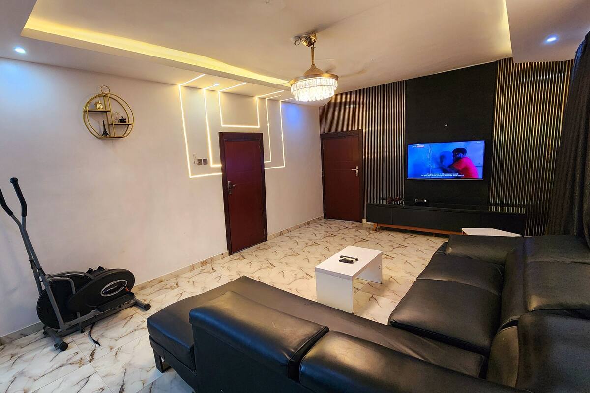 Una sala de estar moderna con un sofá de cuero negro, un televisor y un ventilador de techo.