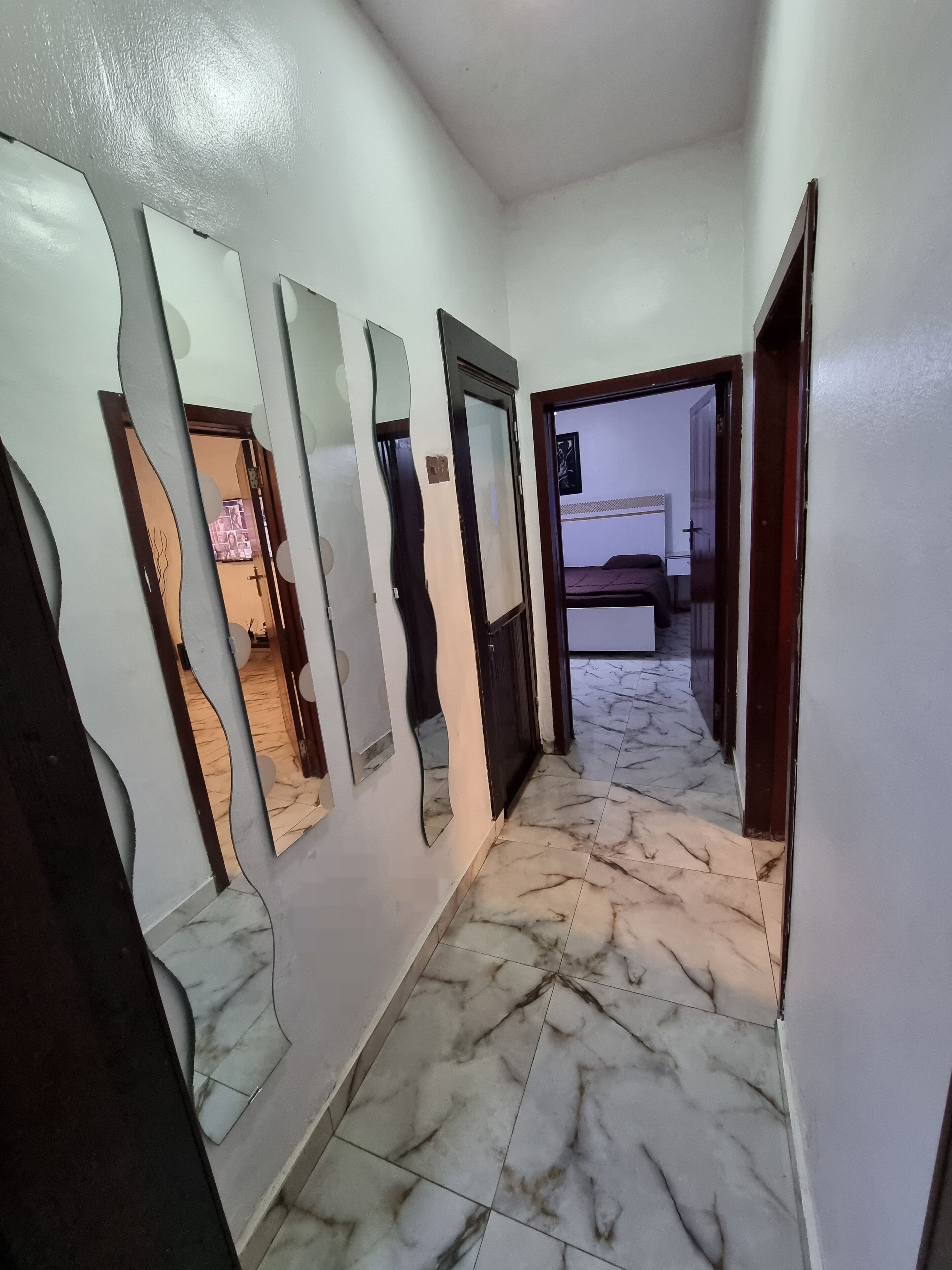 A hallway with marble flooring and multiple mirrors on the walls.