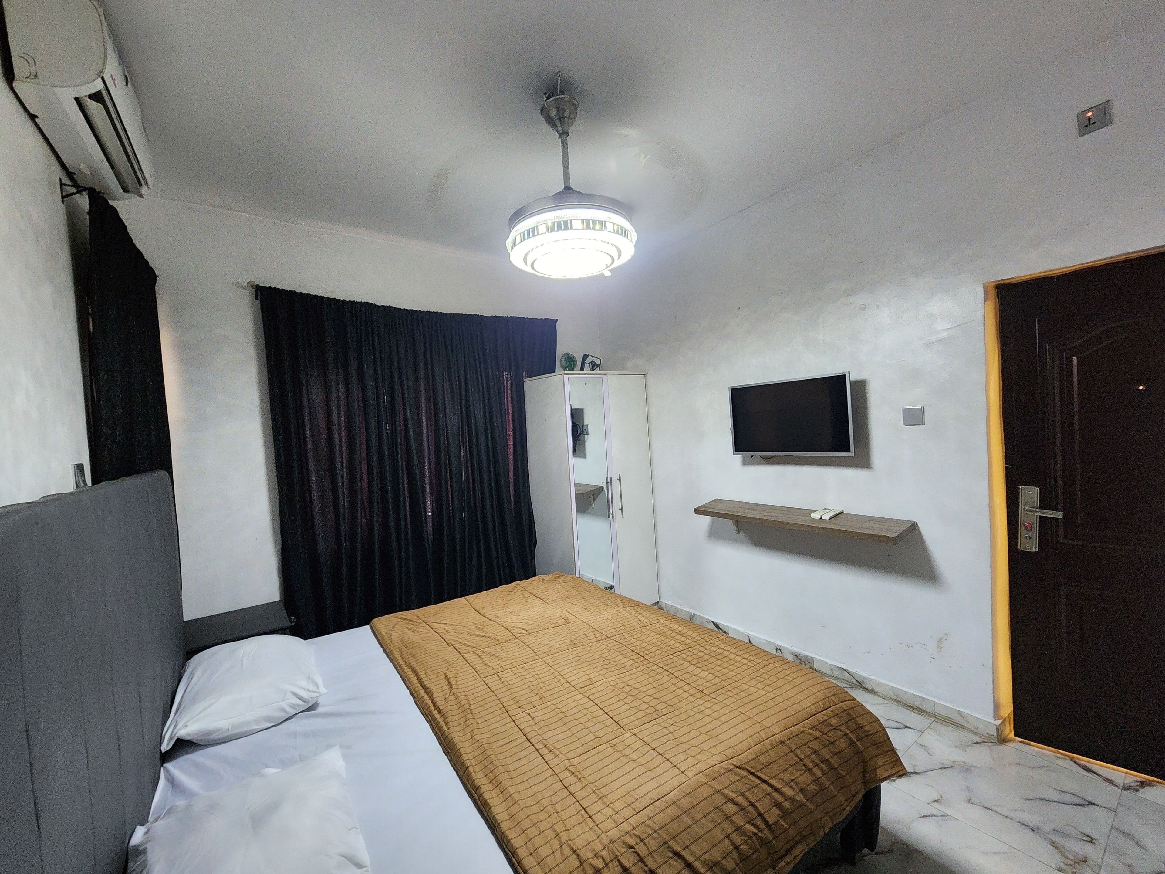 A bedroom with a bed, a ceiling light, a TV, a wardrobe, and a door.