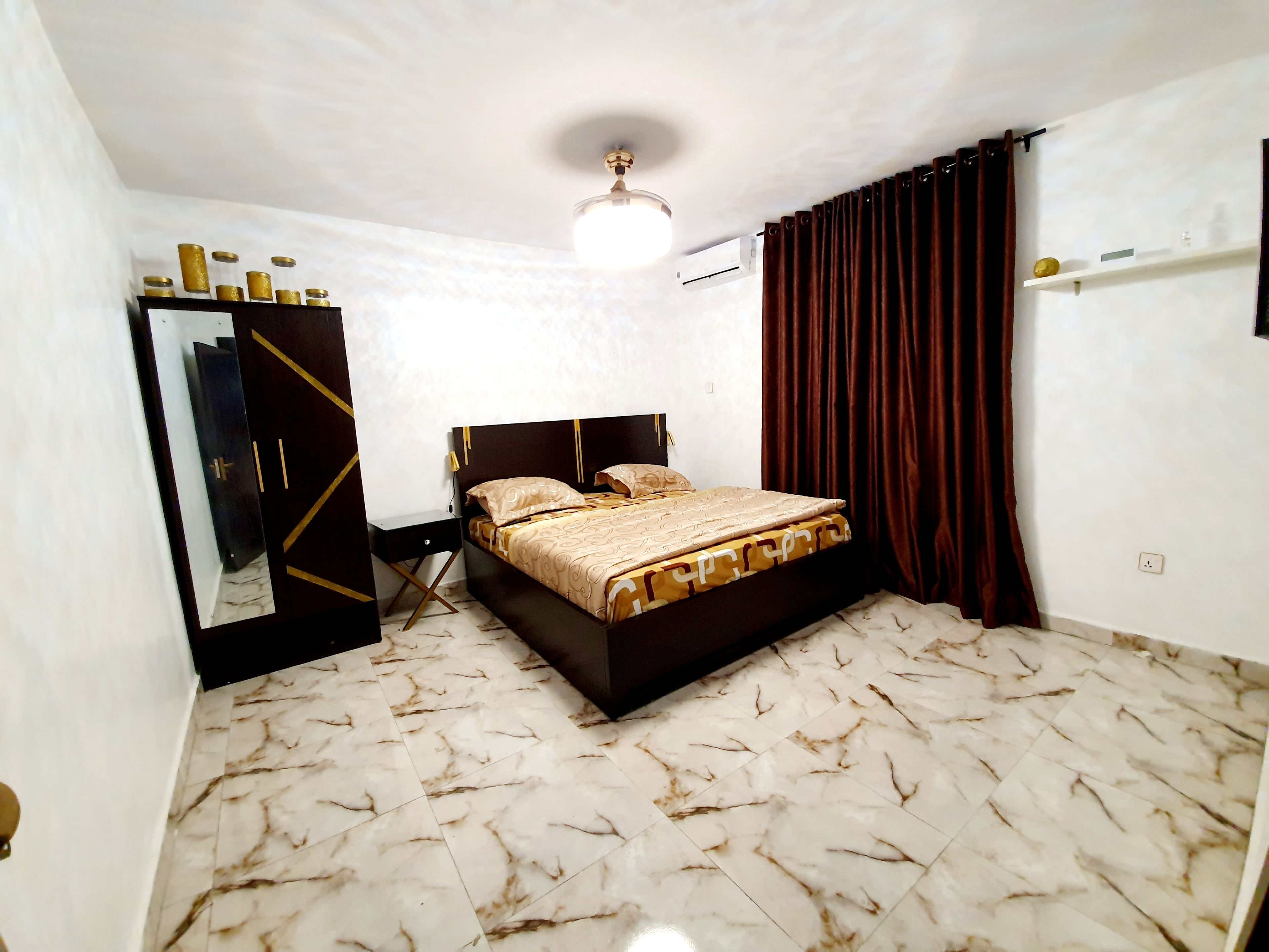 A bedroom with a bed, a wardrobe, a ceiling fan, and a window with curtains.
