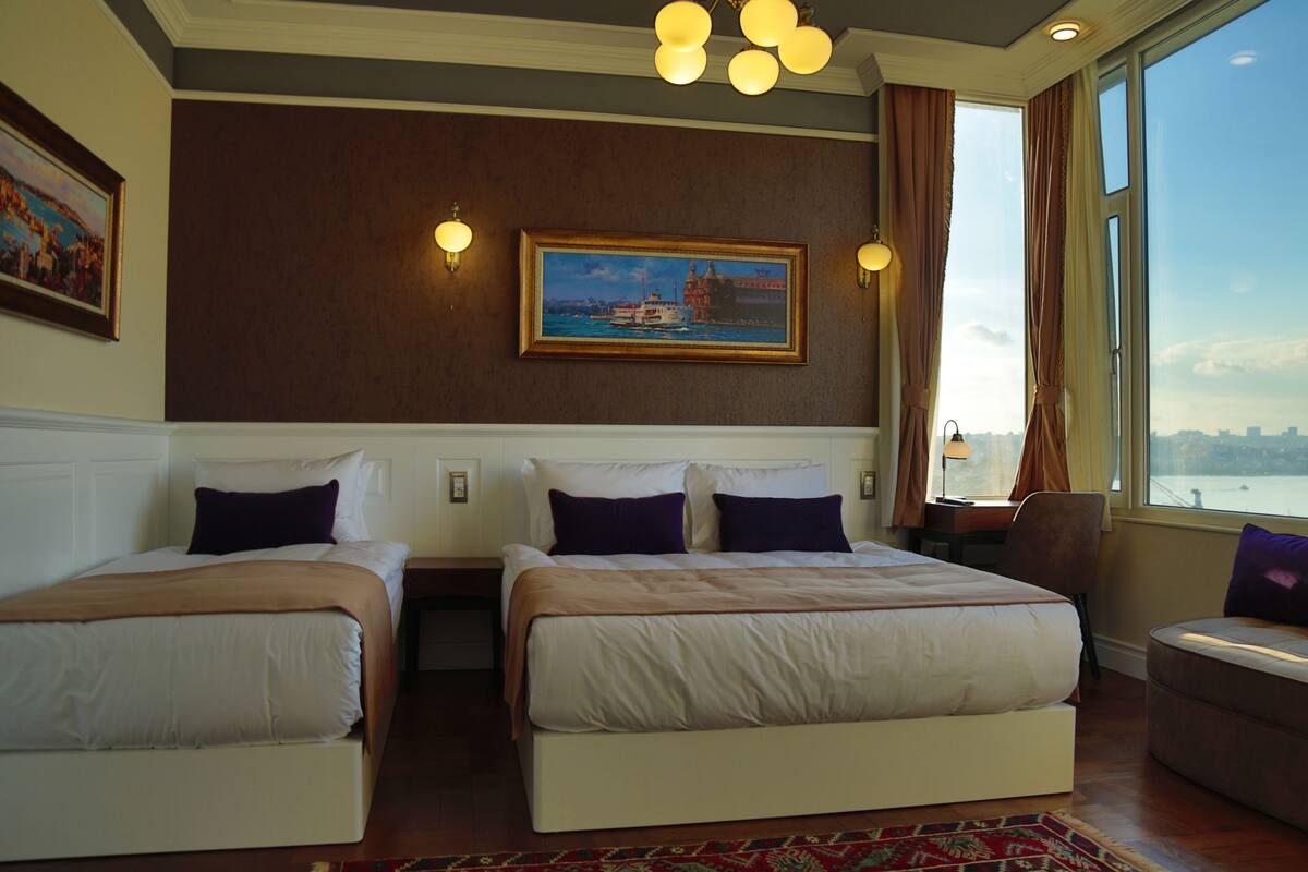 A hotel room with two beds, a large window with a view, and a painting on the wall.