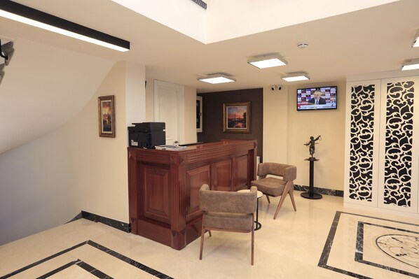 A reception area with a wooden desk, two chairs, a television, and a patterned wall panel. - Art Nouveau Pera (Istanbul)