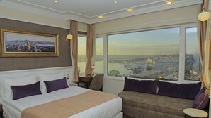 A hotel room with a large bed, a sofa, a view of a cityscape, and a framed picture on the wall. - Art Nouveau Pera (Istanbul)