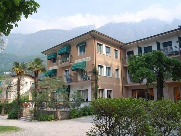 A multi-story building with balconies, a paved courtyard, and a mountainous backdrop. - Hotel Stella Alpina (Malcesine)