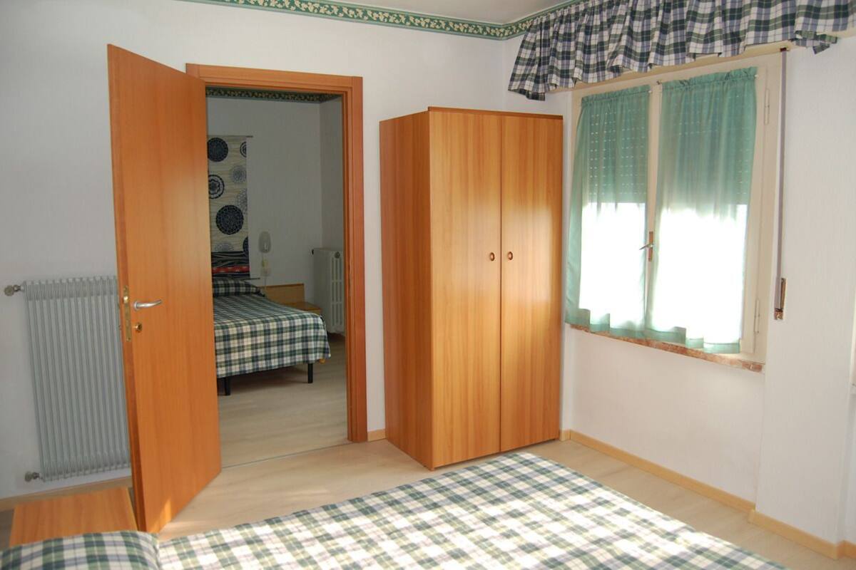 Een slaapkamer met een houten garderobe, een bed met een geruit laken, een radiator en een raam met gordijnen.