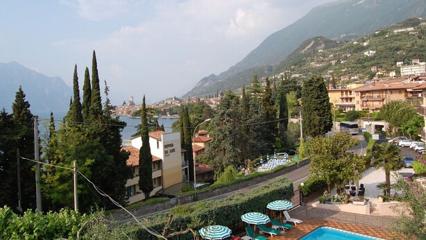 Un hotel junto a la costa con piscina, mobiliario exterior y vistas a la montaña.