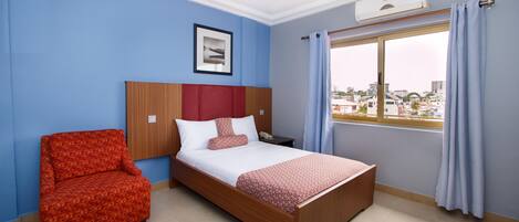 A hotel room with a bed, a chair, a window with curtains, and a city view.