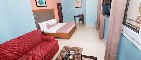 Una habitación de hotel con una cama, un sofá rojo, una mesa de centro y un televisor.