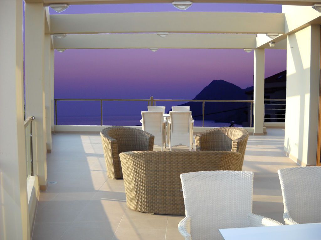 Een balkon met rieten meubilair en uitzicht op zee bij zonsondergang.