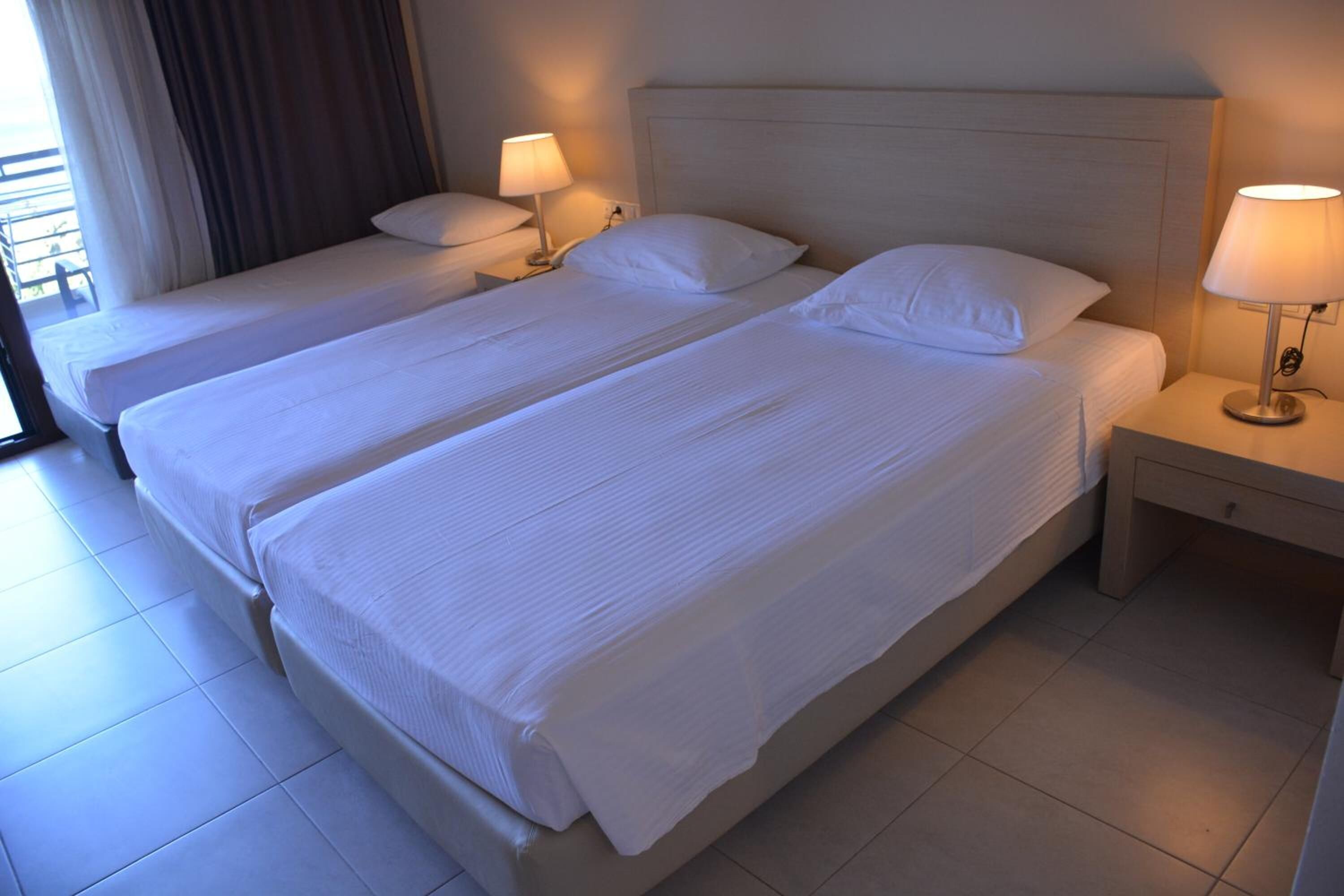 A hotel room with two single beds, each with a pillow and a bedside lamp.