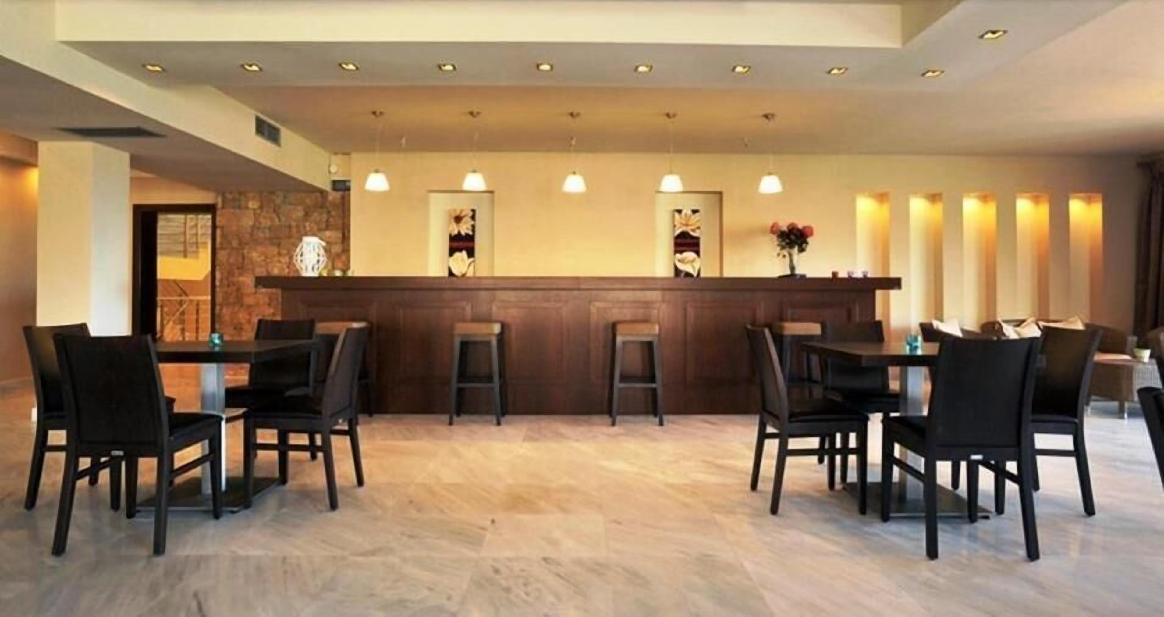 A hotel lobby with a reception desk, bar stools, and black chairs arranged around tables.