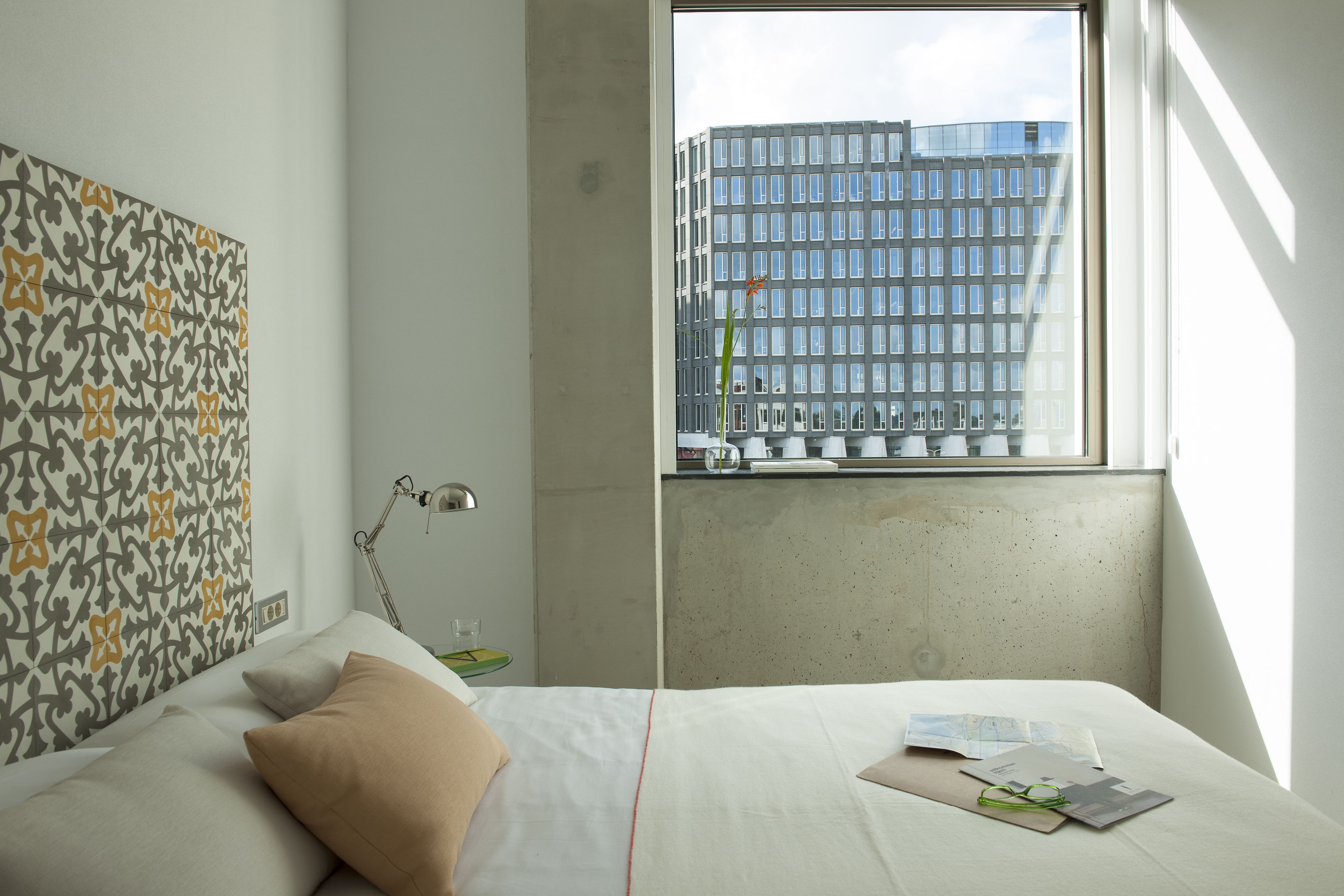 Een moderne hotelkamer met een groot raam, een kamer met een patroon op de muur, en een net opgemaakt bed.