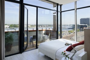 A modern hotel room with large windows, a bed, a desk, and a view of a river and cityscape. - Eric Vökel Boutique Apartments Amsterdam Suites (Amsterdam)