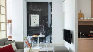 Um espaço de estar moderno com área de jantar, TV fixada na parede e cozinha com tábua de corte de madeira e xícaras.