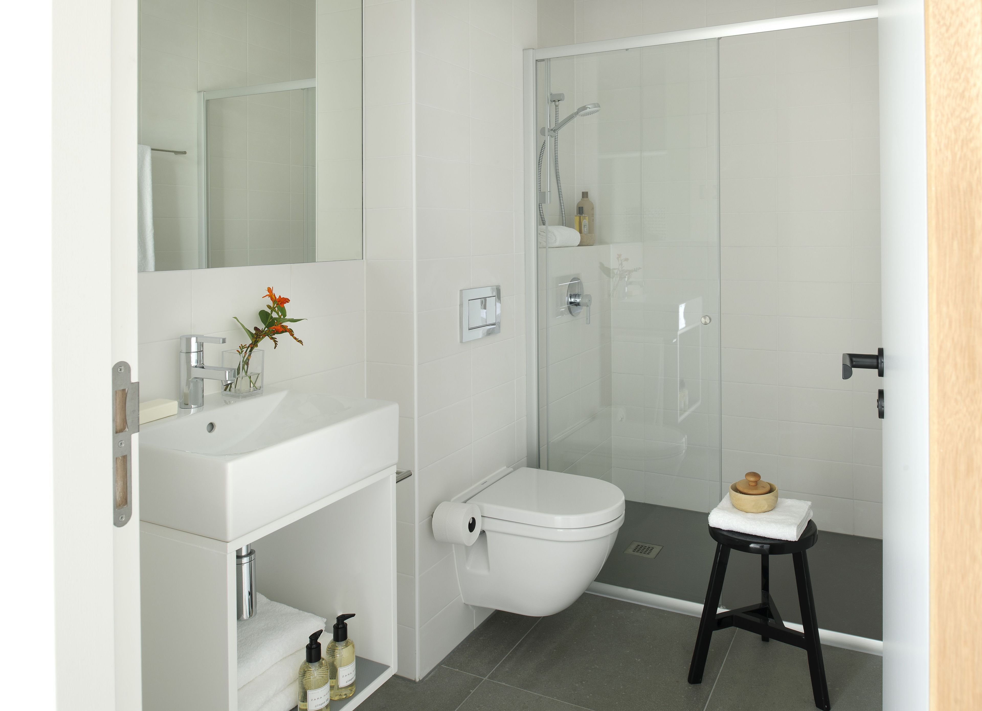 A modern bathroom with a white sink, mirror, toilet, and glass-enclosed shower.