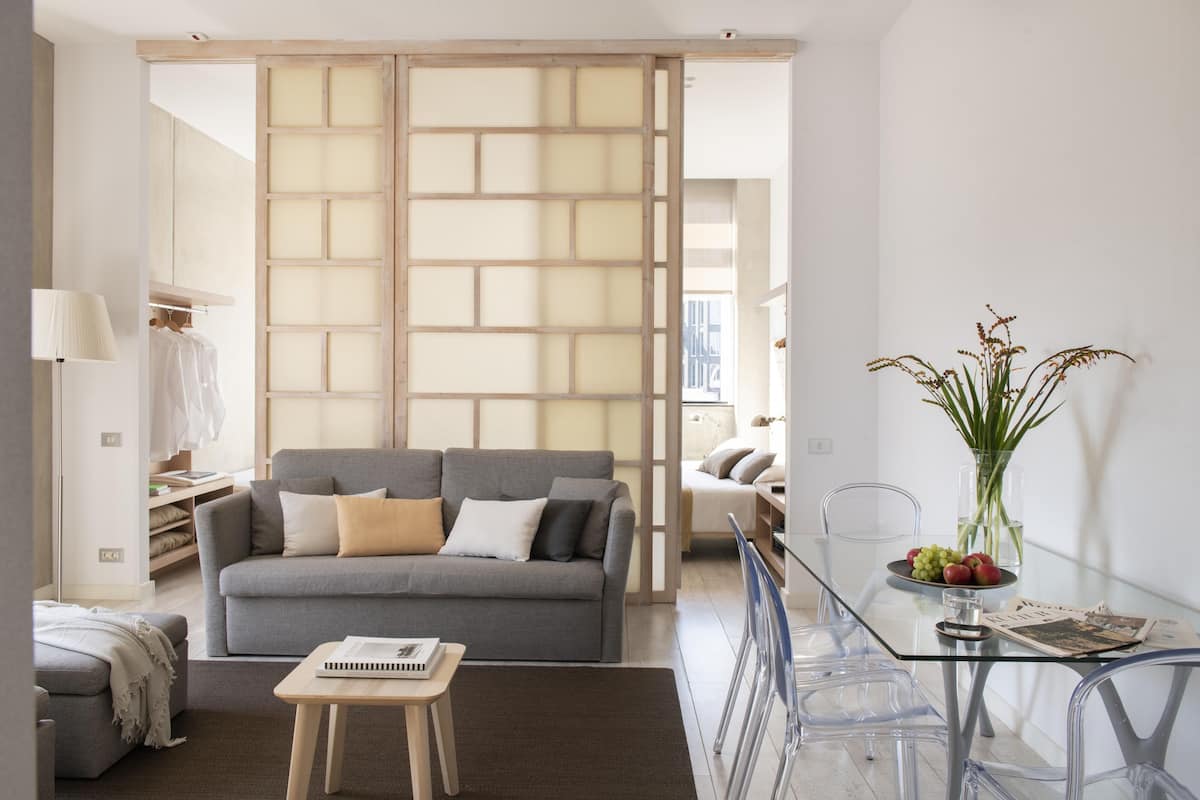A modern living room with a grey sofa, a glass coffee table, and a clear glass partition.
