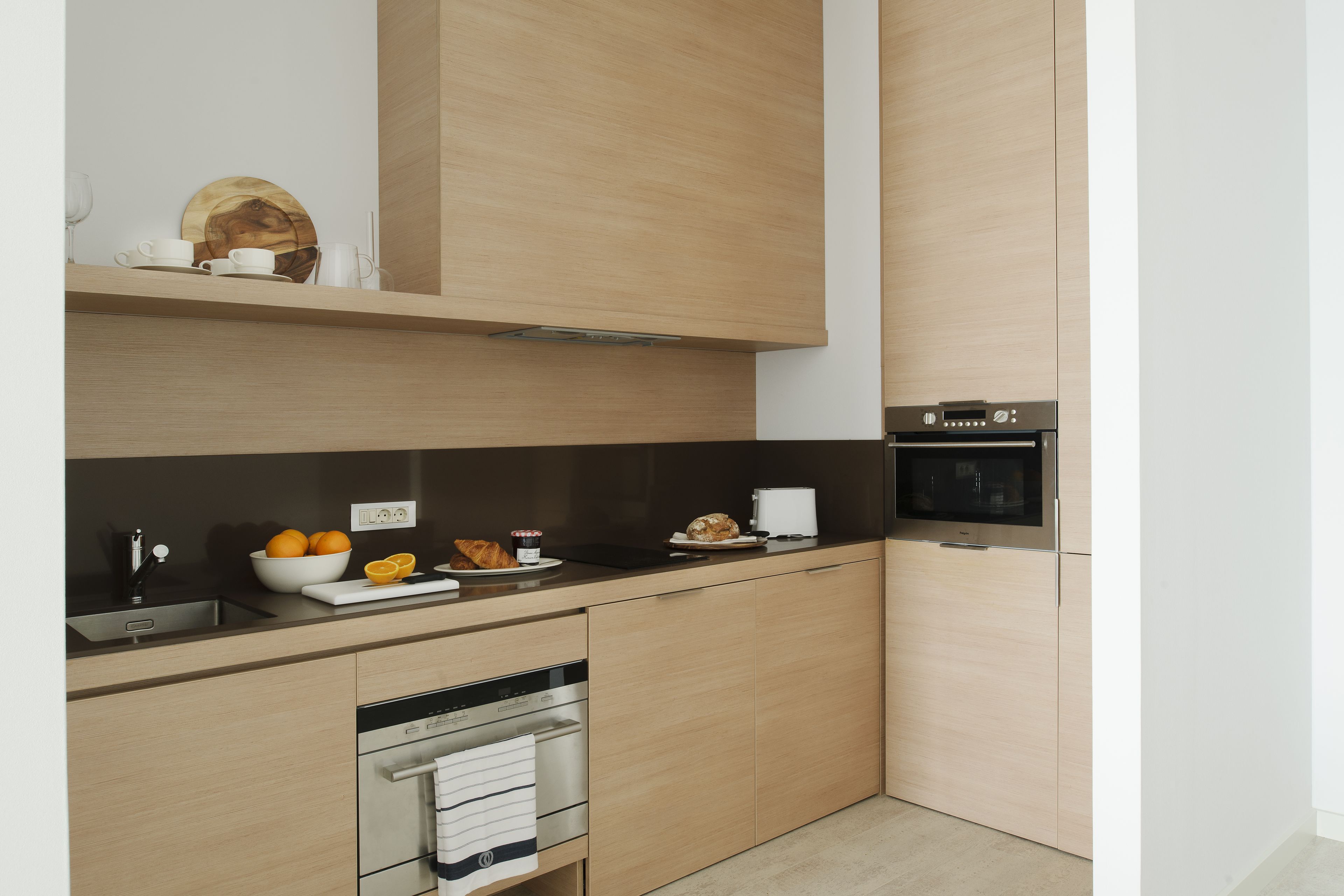 Una cocina moderna con armarios de madera clara, encimera negra y electrodomésticos de acero inoxidable.