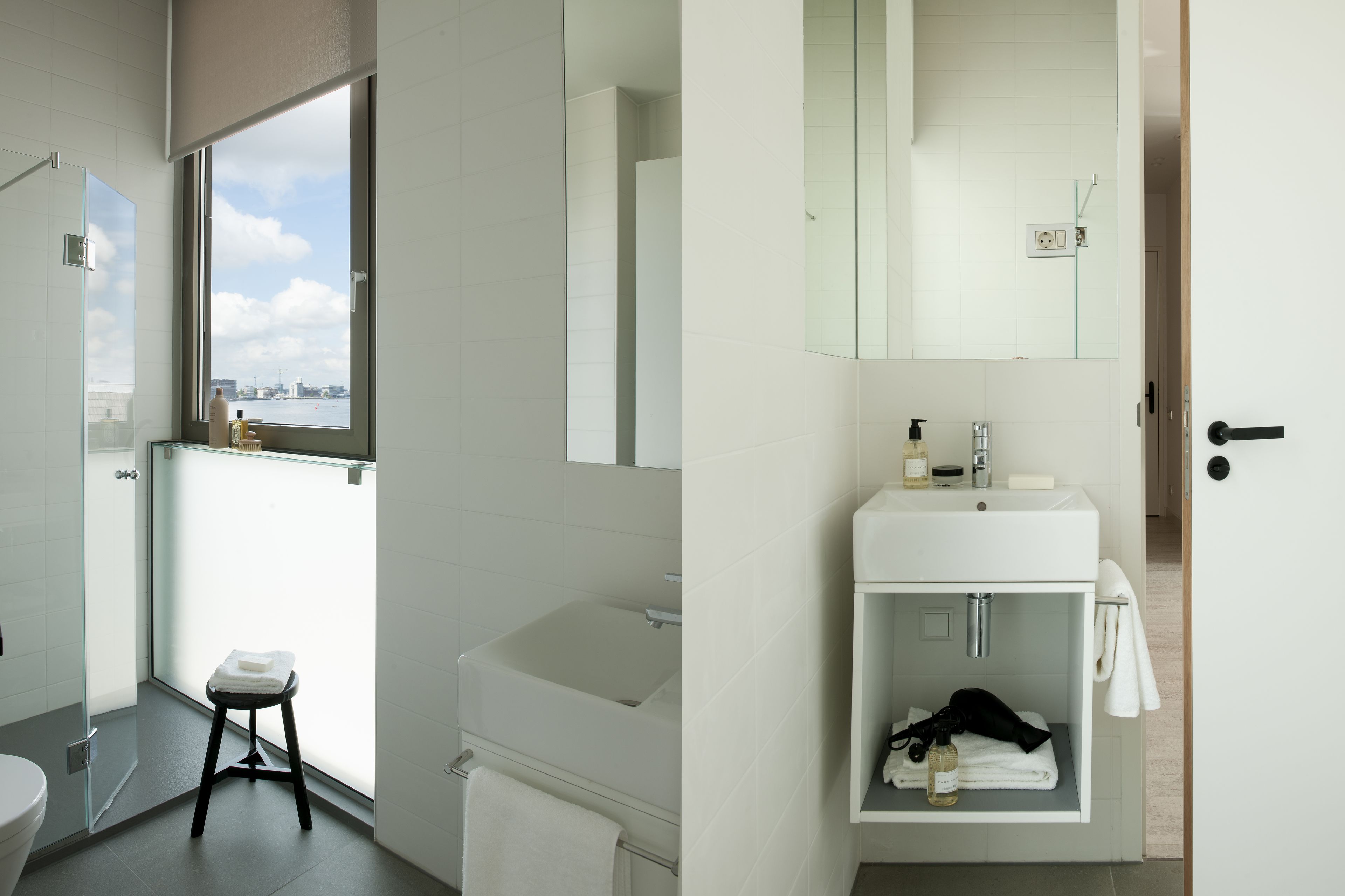 Un baño moderno con un ventanal grande, un lavabo blanco y una cabina de ducha de vidrio.