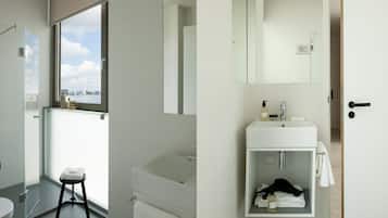 Un baño moderno con un ventanal grande, un lavabo blanco y una cabina de ducha de vidrio.