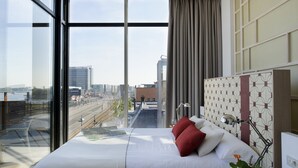 A modern hotel room with a large bed, a view of the cityscape, and a window with a curtain.