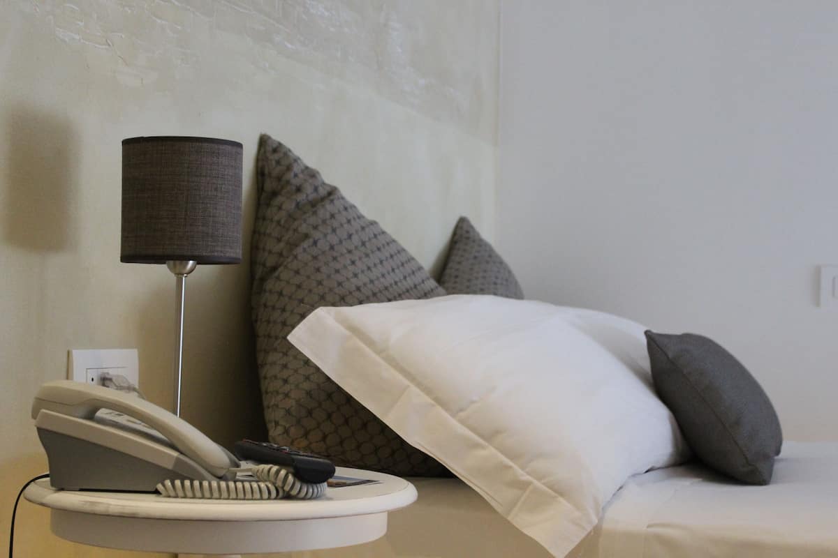Quarto de hotel com cama, abajur, telefone e secador de cabelo sobre uma mesa de cabeceira.
