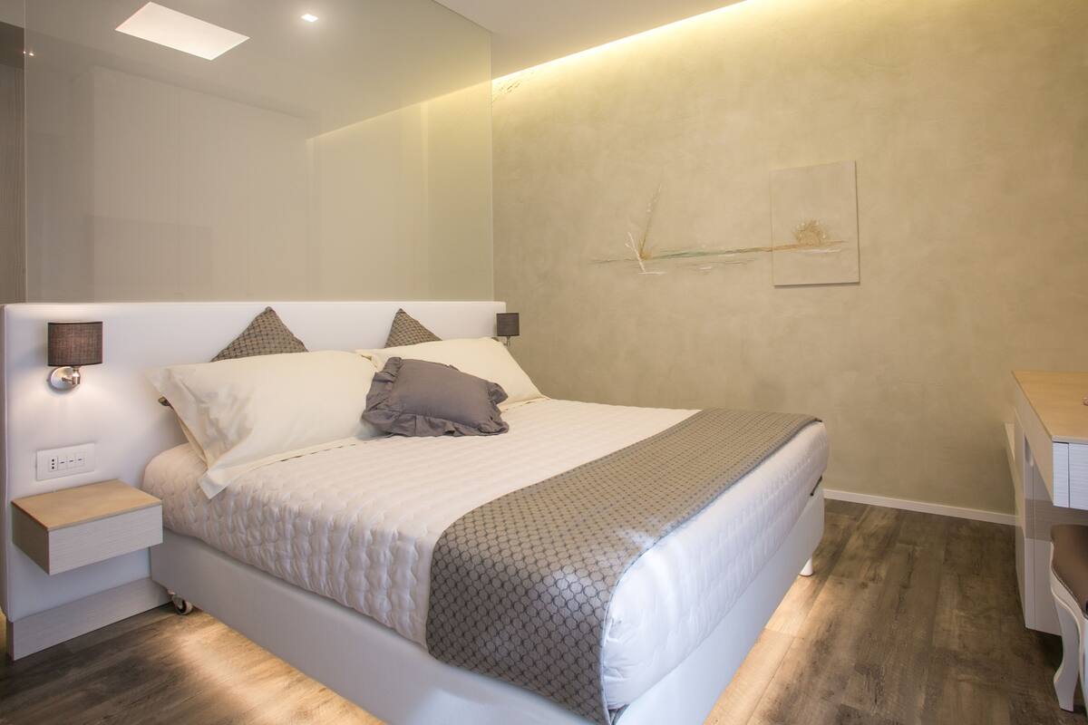 Um quarto moderno com uma cama grande, mesas de cabeceira, uma escrivaninha e uma estante fixada na parede.