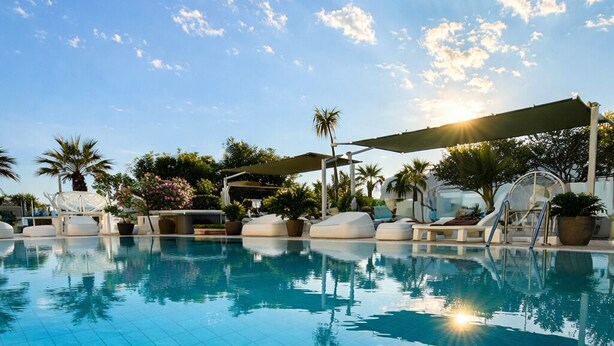 A clear blue pool with tiled flooring, surrounded by lounge chairs and palm trees, under a partly cloudy sky. - Hotel Liberty Beach (Riccione)