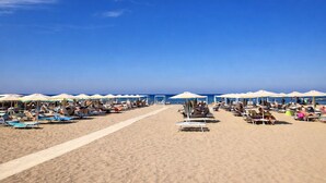 A beach with rows of sun loungers and umbrellas, a clear sky, and the ocean in the background. - Hotel Liberty Beach (Riccione)