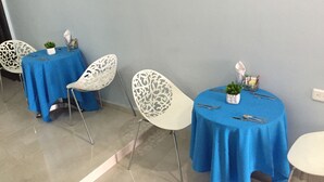 A dining area with tables covered in blue tablecloths, white chairs with intricate designs, and small potted plants. - Hotel Portal de San Antonio (Cartagena)