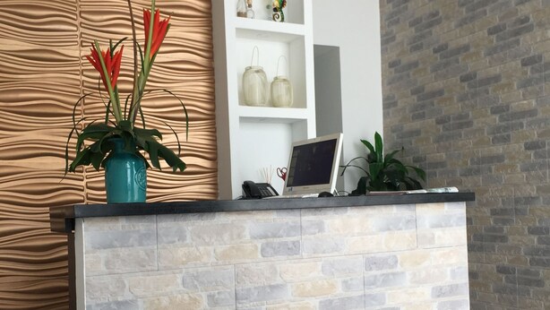 A reception desk with a stone facade, a blue sofa, and a wooden panel wall with a wavy pattern. - Hotel Portal de San Antonio (Cartagena)