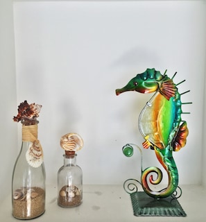 A decorative seahorse sculpture, a glass bottle with a seashell, and a glass jar with a seashell.