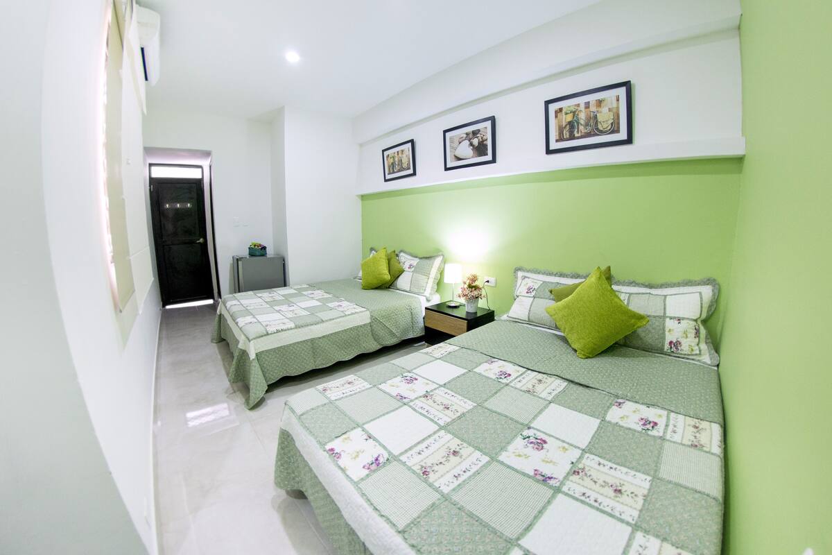 A bedroom with two beds, green bedding, a nightstand with a lamp, and framed pictures on the wall.