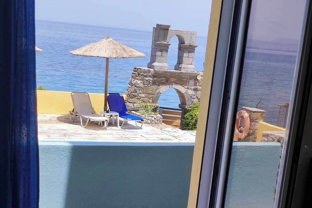 A balcony with a view of the sea, stone archway, and lounge chairs.