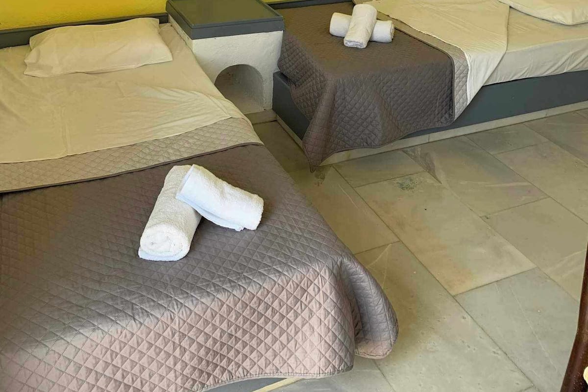 A hotel room with two beds, each with a quilted mattress and pillows, and a nightstand between them.