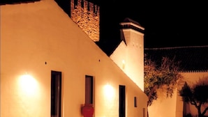 A building with a sloped roof, a stone tower, and a series of illuminated windows. - Herdade da Maxuqueira (Gaviao)